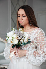 Portrait of a beautiful bride with a bouquet of white roses in her hands in a light interior.