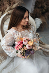 Portrait of a beautiful bride with a bouquet of hydrangea roses and feces in pastel orange color in her hands in a light interior.