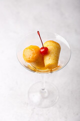 Neapolitan Rum baba (or baba au rum) in a martini glass with a cocktail cherry on a gray background. Small yeast cakes soaked in rum syrup. Traditional Italian pastry. Close-up, selective focus.