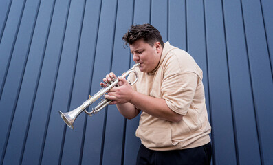 Young street musician playing the trumpet near the big blue wall