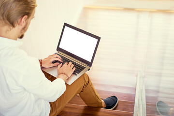 Freelance businessman. Young  man working on laptop while sitting on stairs. Focus on the screen.