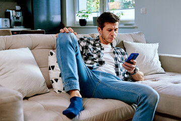 Man using smartphone for browsing social media, resting on sofa at leisure weekend. Male hand touch phone screen, surfing online news