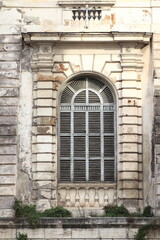 Fototapeta na wymiar Weathered Building Facade Detail with Arch Window and Grey Wooden Shutters in Rome, Italy