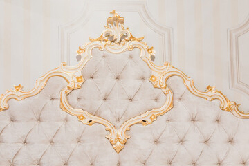 Luxury royal headboard of expensive bed with golden elements and light beige textile - elegant part of bedroom interior
