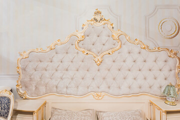 Luxury royal headboard of expensive bed with golden elements and light beige textile - elegant part of bedroom interior