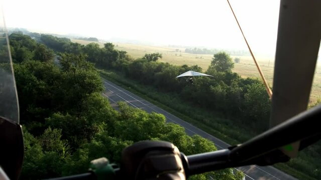 flying on a hang glider with an engine, flying over a paraglider. View from a hang glider. Landing on the road
