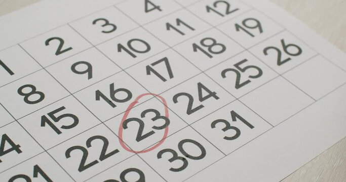 Man's hand Write down the 23th day on the paper calendar using a red pen. Very important date in the calendar. Signing a day on a calendar. Calendar 23th date of the month cut.