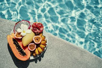 Vacation and diet concept. The plate of tropical exotic colorful fruits near water in swimming pool.