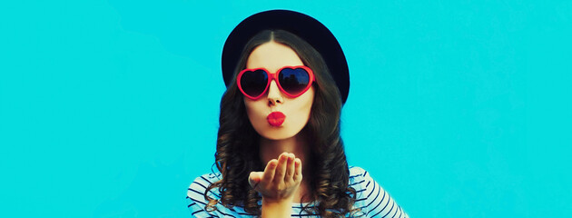 Portrait of beautiful young woman blowing her lips sending air kiss wearing red heart shaped...