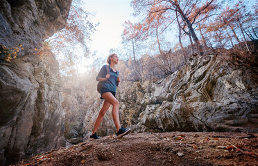 Fototapeta premium Active lifestyle. Trekking and hiking. Young woman with rucksack in the rocks forest.