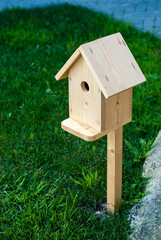A wooden new birdhouse stands on a green lawn. Pine craft.