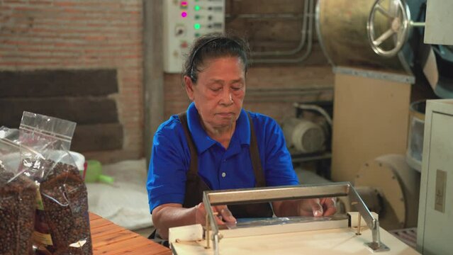 Asian women 74 years old working in a factory. Sealing a bag of coffee beans, coffee roaster process, industrial, worker, Senior woman