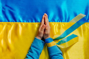 Kids handswith ribbon praying on the Ukrainian flag