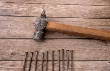an old hammer and ten nails lie on a wooden table