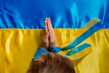 Kids handswith ribbon praying on the Ukrainian flag
