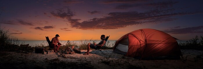 Happy young friends resting by the bonfire near tent.