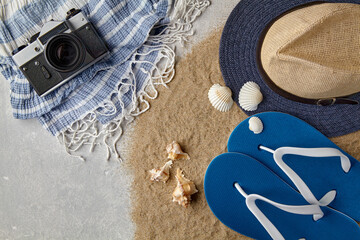 Straw hat, flip flops, seashells, camera and neckerchief on scattered sea sand