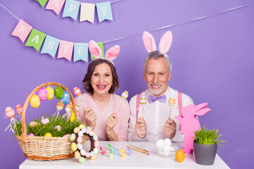 Photo of funny positive people hold craft eggs stick enjoy festive isolated on purple color background