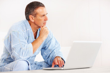 Retired man in bathrobe with laptop looking at copyspace. Portrait of a retired man in bathrobe with laptop looking at copyspace. - obrazy, fototapety, plakaty