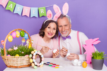 Photo of two funny elderly grandparents paint collect eggs prepare festive isolated on purple color background