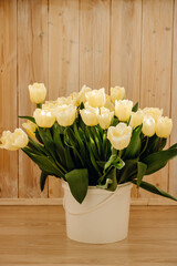 Bouquet with beautiful yellow tulips on a wooden light background. Buds of yellow tulips in a white bucket