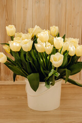 Bouquet with beautiful yellow tulips on a wooden light background. Buds of yellow tulips in a white bucket