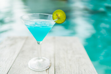 Glass of cocktail decorated with slice lime with swimming pool background
