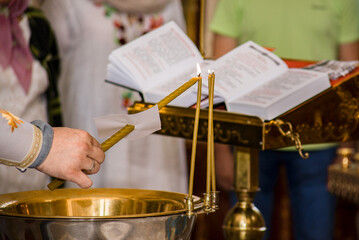 a candle in the hands of a priest lights another, in the background of the bible, there is a service in the church