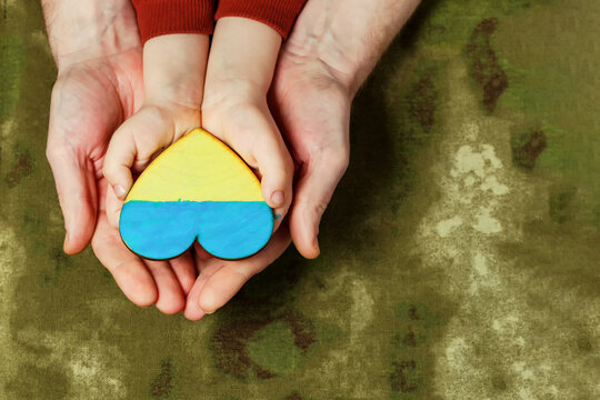 Men's palms support the hands of a child. Heart in the hands of a child, painted in the colors of the flag of Ukraine