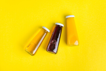 Bottles with yellow and red liquid halthy beverage on yellow background. Orange apple cherry juice