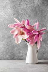 beautiful bouquet of pink magnolia flowers in vase on gray background. vertical orientation