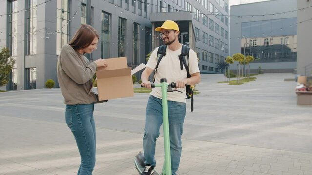 Courier delivering a parcel on an electric scooter. Smiling young girl opening a carton box and pulls out shoes. Delivery from an online clothing store. Shoe delivery. Online shopping