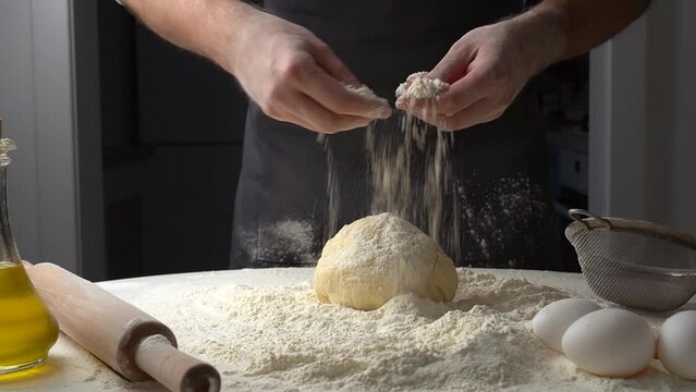 Male hands kneading dough with flour on kitchen table. Chef cooks dough in slow motion front view
