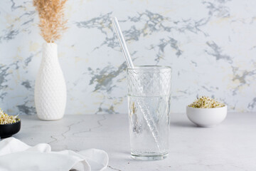 A glass of clean water and a glass straw for drinking on a light table. Diet organic lifestyle