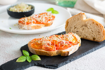 Ready to eat bread sandwich with sundried tomatoes and clover and alfalfa sprouts on a slate on the table. Diet organic food