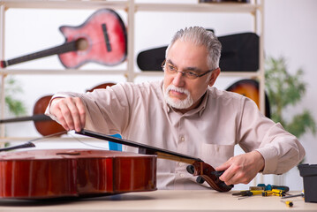 Old male repairman repairing musical instruments at workplace
