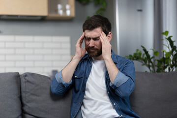The man is sick at home, has a severe headache, sitting on the couch in the kitchen