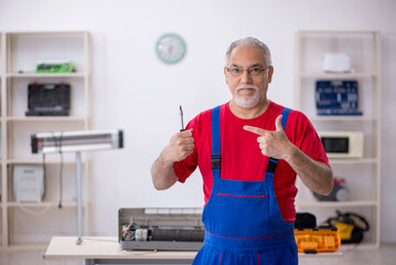 Old repairman repairing air-conditioner at workshop