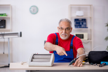 Old repairman repairing heater at workshop