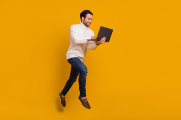 Photo of positive pretty guy wear white pullover jumping high writing modern device isolated yellow...