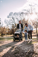 Multi-ethnic male gay couple walking with their little daughter in the park. Modern family concept. Vertical