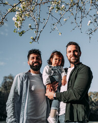 Portrait of a male gay couple with their young daughter in a park. Modern family concept.