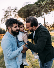 Gay couple of men having fun tickling their daughter who laughs.