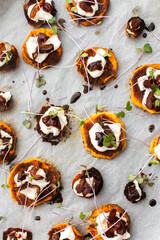 Oven baked sweet orange sweet potato wedges with yogurt and dates sprinkled with microgreens, sweet potato on parchment paper on a baking sheet, top view