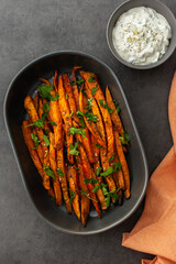 Oven baked orange sweet potato wedges with spices and oil in an oval ceramic dish, avocado sauce with yoghurt and spices