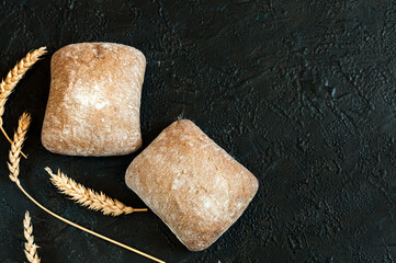 Italian ciabatta bread in the form of small two square buns on a black concrete background with...