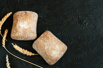 Italian ciabatta bread in the form of small two square buns on a black concrete background with copy space. Selective focus, natural light