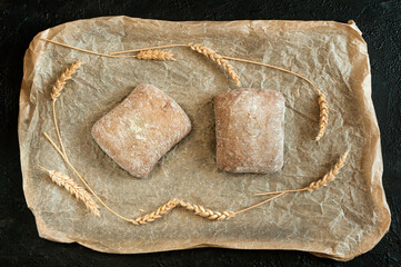 Buns on parchment with grains and ears of corn. Mini Italian ciabatta. Top view, selective focus. Daylight