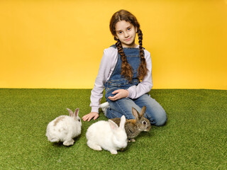 Little schoolgirl is lying down playing with the bunnies in the studio, yellow background.