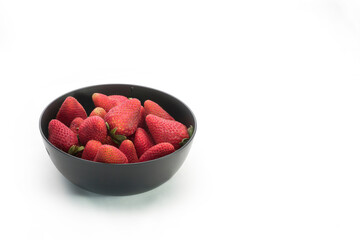 Closeup of a stack of strawberries in a black bowl, on white background with copy space.